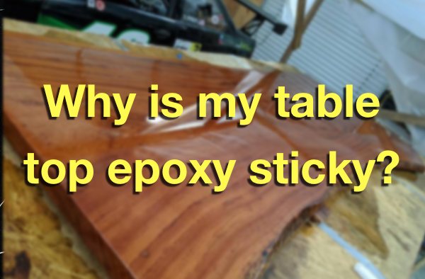 A blurred photo of a wooden epoxy table top with a sticky surface. There's a text overlay that says "Why is my table top epoxy sticky?"